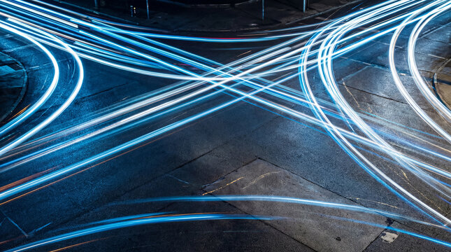 High-angle view of a busy intersection at night, showing light trails from moving vehicles creating a vibrant, futuristic cityscape.