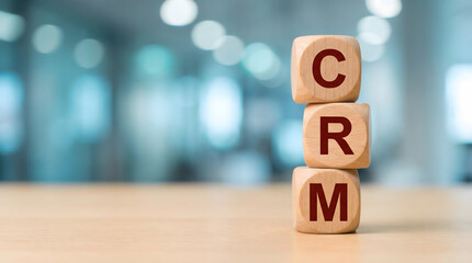 Customer Relationship Management CRM concept shown with wooden blocks on a clean desk in a modern office setting with blurred ligh