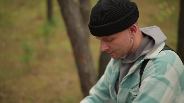 White outdoor guide examining forest plants with open palm, gestures toward fern and moss, adjusts backpack straps, inquisitive expression, soft filtered light among pine trunks, intimate nature