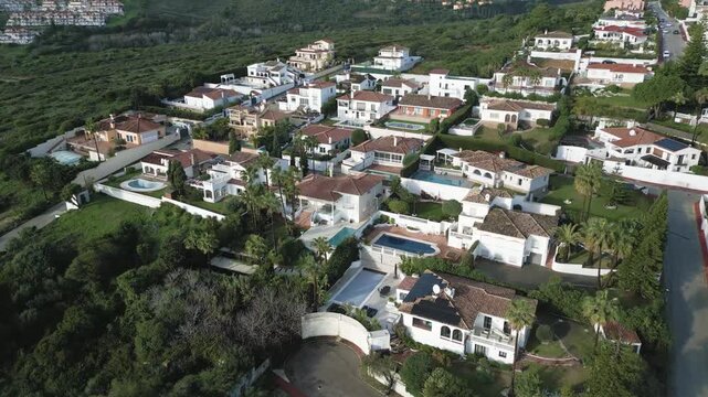 Drone footage capturing a Mediterranean neighborhood of villas and greenery on the Costa del Sol, with mountains and coastline in the distance.