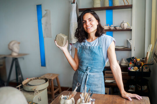Latin woman ceramic artist shaping clay in pottery studio, working with apron, craft creative activity concept