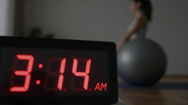 Digital alarm clock displaying 3 14 AM next to a woman with an exercise ball