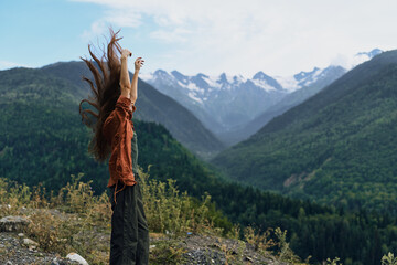 Fototapeta premium A person stands on a rocky overlook in a vast mountain landscape with arms raised, embracing freedom and adventure, capturing a triumphant moment and a strong connection with nature