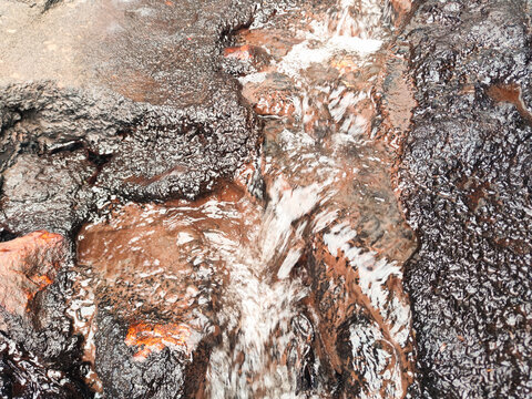 Close-up of water flowing over dark stones, revealing raw textures and organic patterns shaped by motion, moisture, and natural erosion