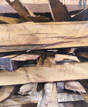 Close-up of stacked rough wooden planks showing raw natural texture, saw marks, bark edges, and rugged lumber surface used for carpentry, woodworking, and construction material supply