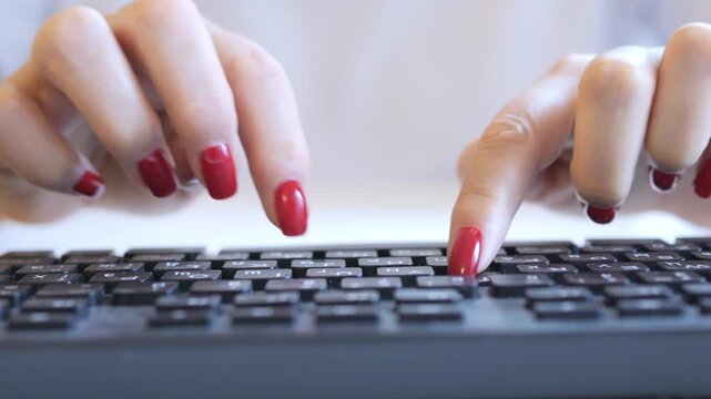 Woman is typing on a keyboard with her fingernails painted red. She is using the shift key to type