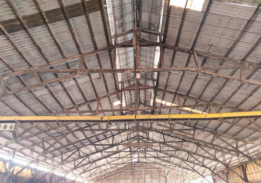 Symmetrical view of an old industrial warehouse roof with metal sheets, wooden beams, rustic textures, and strong architectural industrial structure