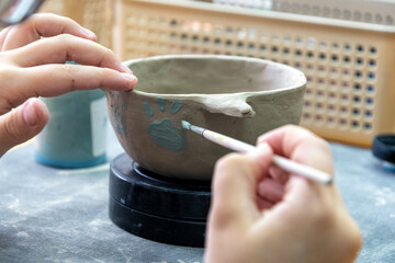 Child's hands carefully paint a handmade clay pot with paw print design. Creative art workshop activity, fostering development and education