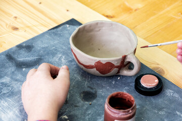 Hand painting a unique, handmade clay cup with terracotta paint in a pottery workshop. Capturing creativity, learning, and artistic skill