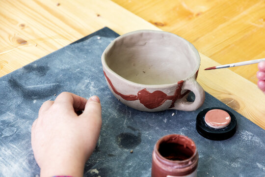 Hand painting a unique, handmade clay cup with terracotta paint in a pottery workshop. Capturing creativity, learning, and artistic skill