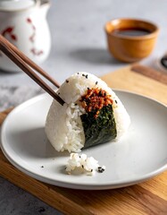 Rice ball with seaweed, on white plate and wooden board, plus soy sauce and chopstick accents