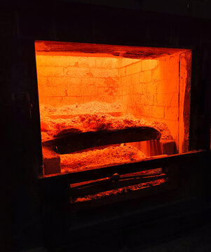 Glowing interior of an industrial furnace revealing extreme heat, combustion residue, and refractory brick walls used in heavy manufacturing and thermal processing