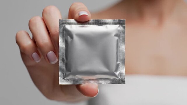 Holding Unopened Condom in White Hand. Suitable for Sexual Health, Safe Sex, Education and Relationships Communication Resources.
