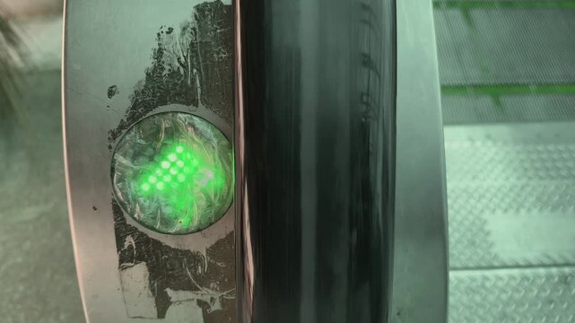 Closeup of green arrow direction indicator glowing on escalator side panel, worn metal surface and moving steps nearby, showing guidance system inside railway station