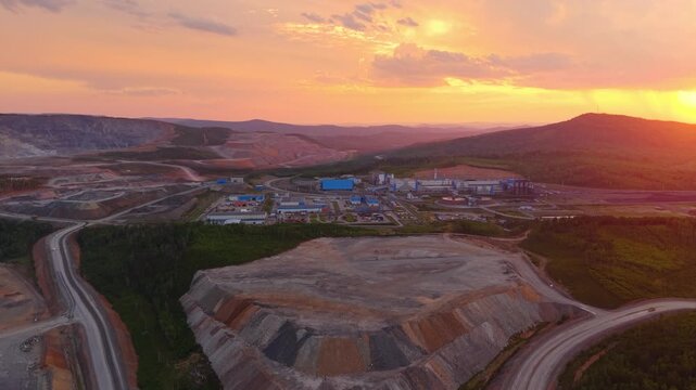 Aerial view of large open pit mining site with gold, copper and iron ore processing plant factory at sunset in remote landscape. Industry quarry with mineral.