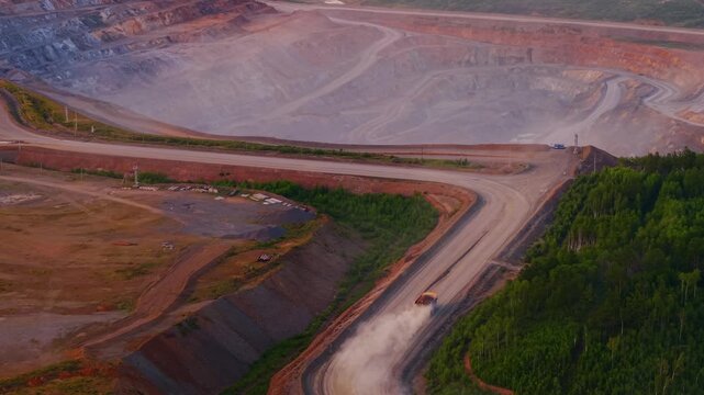 Aerial view big yellow truck moving of expansive open pit mine for gold ore or nickel, zinc in industry landscape, sunset time.