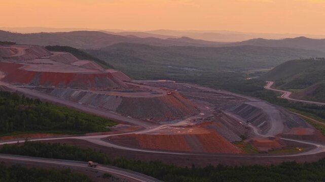Majestic aerial view of vast open pit mine in mountainous landscape at sunset.