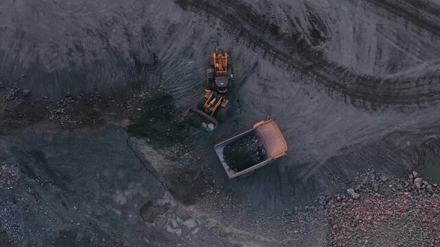 Aerial view excavator loads golden ore into truck dump, mining site.