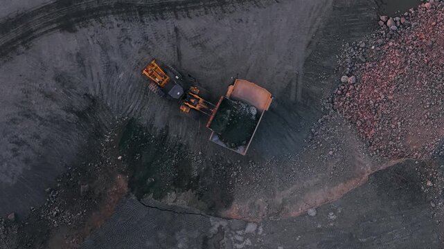 Excavator loads golden ore into truck dump, Aerial view mining site.