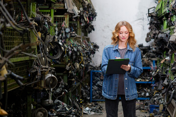 Woman carefully inspecting a junkyard with pen and clipboard