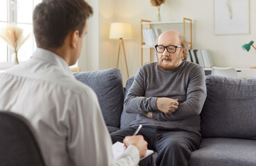 Male young professional psychologist doctor making notes consulting senior elderly man patient...