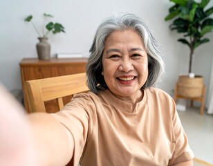 Smiling senior woman, gray hair, takes selfie. Indoor setting, plants, wooden furniture visible in background