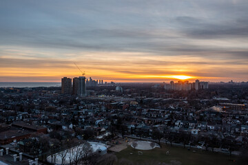 Naklejka premium Toronto cityscape showing residential homes and high rise buildings illuminated by the setting sun casting warm orange hues across the sky above an outdoor skating rink and park
