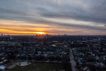 Naklejka premium Toronto skyline and sprawling residential neighborhoods bathed in warm orange sunset light, dramatic clouds over urban and suburban development stretching to the horizon at dusk