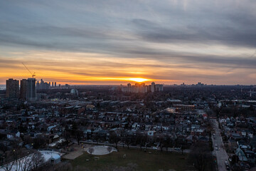 Naklejka premium Toronto cityscape featuring residential neighborhoods and an urban park, bathed in the warm glow of a setting sun painting the sky with orange and yellow hues, highlighting the vast city expansion