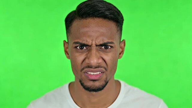 A young man with a puzzled expression on his face, looking directly at the camera with a green screen background, appearing confused or unsure.
