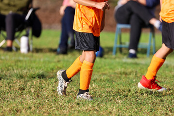 Fototapeta premium View of a 6 yr old boy with bright orange uniform playing soccer on the field.
