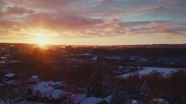 Hamilton Sunset over a quiet neighbourhood after a snowstorm. Fresh white snow blankets the trees and houses as vapor billows from chimneys and rooftops of buildings. The cold skies are dramatic.