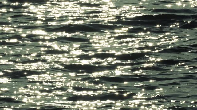 Sparkling silver sun reflections on rippling water surface