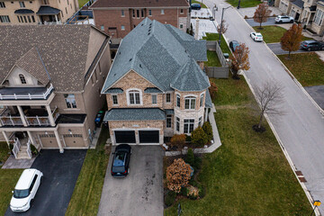 New construction luxury homes creating a modern suburban neighborhood street with cars parked in driveways and on the road, surrounded by lawns and some autumn trees
