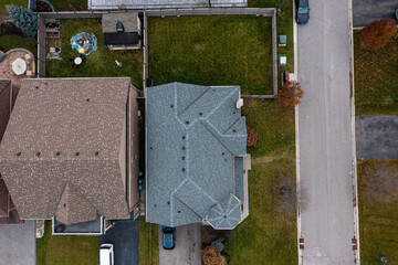 Residential neighborhood with houses, shingle roofs, green yards, and a street with parked cars, captured from an overhead perspective showing urban development