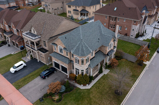Large detached home with intricate stone and brick facade, multiple gables and grey shingle roof, nestled among modern residences in a quiet brampton, ontario suburb