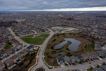 Suburban housing development showing a dense residential community with detached houses, streets, a park, and a naturalized pond area under a cloudy sky in brampton, ontario, canada