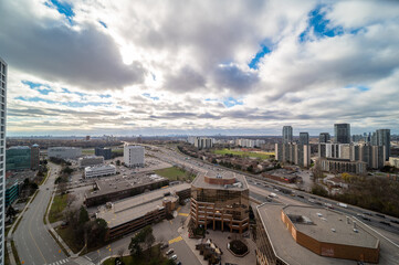 Naklejka premium Expansive view over a vibrant urban landscape featuring high rise buildings, busy highways with moving traffic, and a large city skyline stretching towards the horizon under a cloudy sky