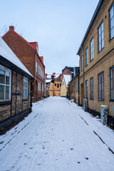 Empty narrow cobblestone street covered in snow between historic brick buildings in winter in Lund Sweden
