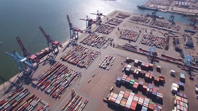 A dynamic aerial time-lapse captures the rhythmic flow of a global port, where synchronized cranes and cargo ships move against a dramatic sky at golden hour.