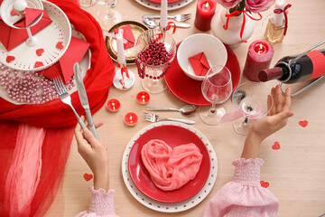 Naklejka premium Young woman sitting at served table with folded napkin, burning candles and glasses in dining room. Valentine's Day celebration