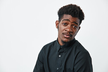 Obraz premium Young black man with dark skin and afro hairstyle wearing black shirt posing with thoughtful expression on white background. Male model with casual style and natural look.