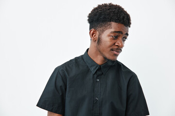 Obraz premium Young African American man with dark skin and curly hair wearing black shirt looking sideways on white background. Portrait, casual style and thoughtful expression in studio.