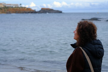 Fototapeta premium A woman walks along the sea, a winter sunset, with calm water, in the background a coastal village and rocks