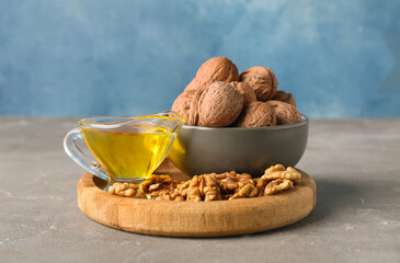 Gravy boat of fresh walnut oil and bowl with nuts on grey table