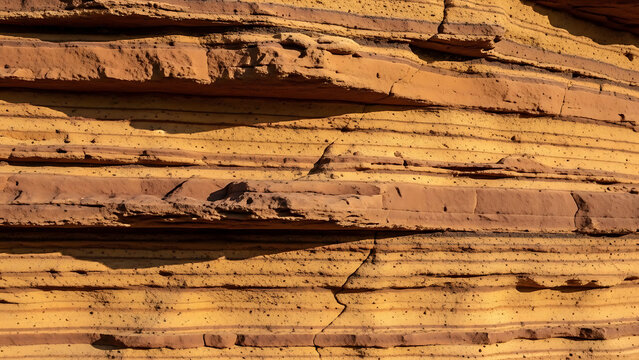 Close up of rough sedimentary rock strata with deep cracks and jagged edges highlighting the geological erosion and natural earth textures.