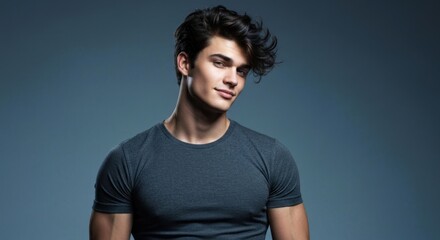 Fototapeta premium Handsome young man in gray tee, looking slightly down, with dark wavy hair, studio background