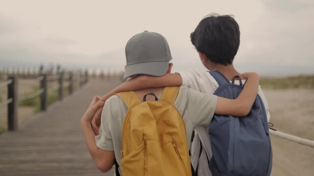 Two boys with backpacks walking on a boardwalk, one boy putting an arm around the other's shoulder, symbolizing friendship, support, and childhood adventure