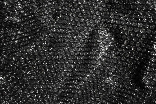 Textured plastic bubble wrap packaging overlay, close-up image of crumpled black bubble wrap.