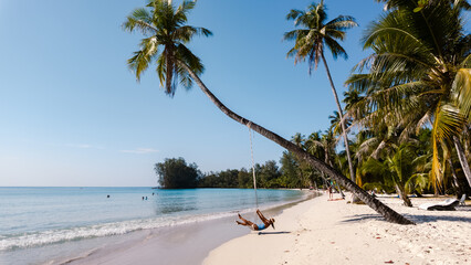 Swaying gently on a swing placed beneath tall palm trees, a traveler enjoys the serene beauty of...